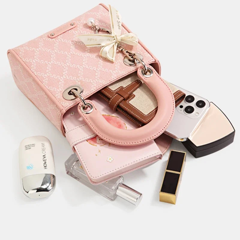 Open pink Clarisse Bow Jacquard Handbag filled with daily essentials like phone, wallet, and cosmetics, demonstrating its practical storage capacity.