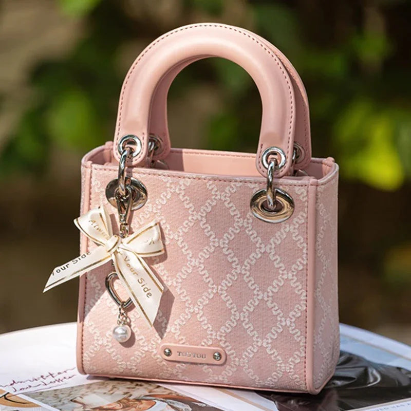 Close-up of pink Clarisse Bow Jacquard Handbag with heart charm and ribbon, emphasizing its luxurious jacquard fabric and polished metal details.
